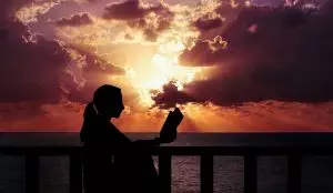 silhouette of woman reading at the ocean in front of a sunset